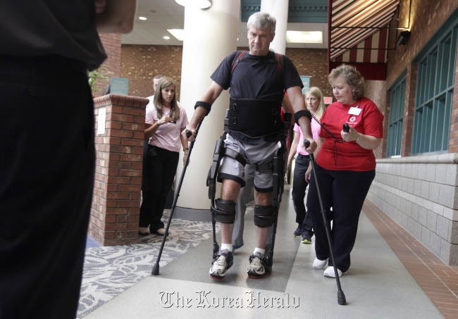 With guidance from physical therapists Nancy Hicks (right) and Nicolle Lang (directly behind), David Ayscue, 56, wears a robotic exoskeleton to help him walk at WakeMed Rehab in Raleigh, North Carolina, on Sept. 27. (Raleigh News & Observer/MCT)