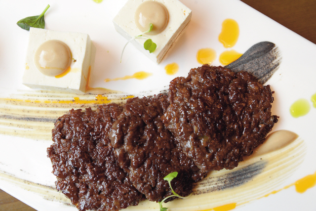 Dudukansang’s chargrilled bulgogi-tofu-kimchi trio pairs the juicy sweetness of marinated beef patties with garlic-bean curd sauced house-made tofu and the tart tang of aged kimchi for a complex and thoroughly enjoyable dish. (Ahn Hoon/The Korea Herald)