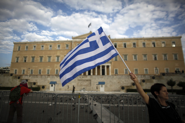 A demonstrator waves a Greek national flag ahead of a protest against a visit by Angela Merkel, Germany’s chancellor, opposite the Greek parliament building in Athens on Oct. 9. (Bloomberg)