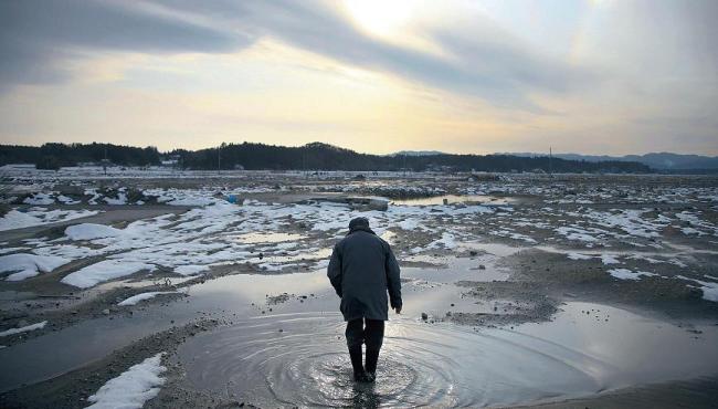 Kazushige Hayashi walks through puddles of water at the site of where his house stood before the March 11 earthquake and tsunami in Minamisoma City, Fukushima Prefecture, Japan, Sunday. (Bloomberg)