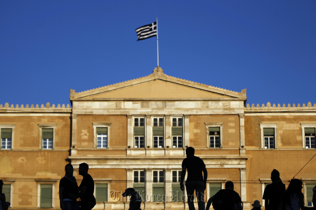 Pedestrians stand in front of the Greek parliament building as the country’s national flag flies from the top in Athens. (Bloomberg)