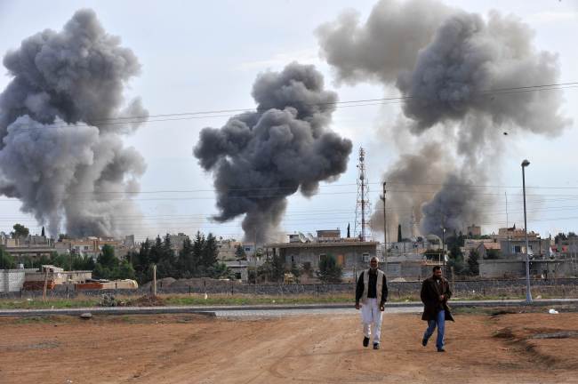 A picture taken from the adjacent Turkish border town of Ceylanpinar shows people walking in front of smoke after a Syrian aircraft bombed the strategic border town of Ras al-Ain, on Tuesday. (AFP-Yonhap News)