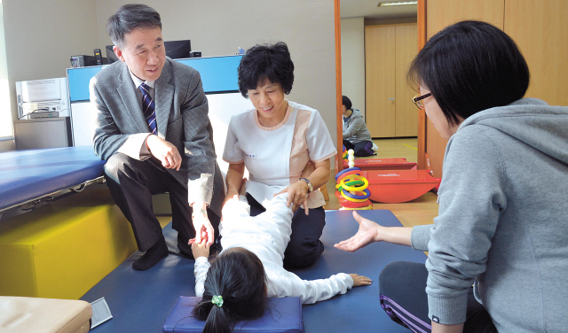 Paik Kyung-hak (left), executive director of Purme Foundation, holds the hand of a child receiving physiotherapy at Purme Rehabilitation Center in Jongno, Seoul. (Kim Myung-sub/The Korea Herald)