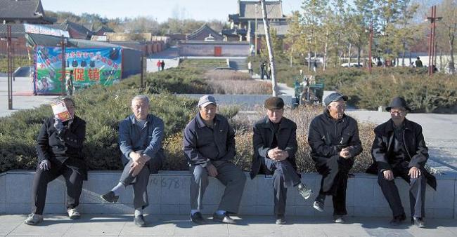 A woman covers her face with a leaflet as she sits with a group of elderly men near a temple in Xilinhot in northern China’s Inner Mongolia. In the small town, a deputy chief paid three times an average urban resident’s annual salary to become its police chief. (AP-Yonhap News)