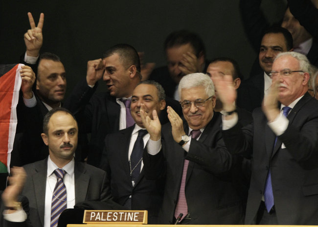 Members of the Palestinian delegation react as they surround Palestinian President Mahmoud Abbas (center), who applauds during a meeting of the United Nations General Assembly after a vote on a resolution on the issue of upgrading the Palestinian Authority’s status to non-member observer state passed in the United Nations in New York. (AP-Yonhap News)