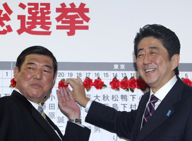 Japan’s main opposition leader Shinzo Abe (right) of the Liberal Democratic Party, and the party Secretary-General Shigeru Ishiba pose for photos as they place a rosette on the name of one of those elected in parliamentary elections at the party headquarters in Tokyo on Sunday. (AP-Yonhap News)