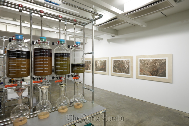 Photos of the autumn landscape at Mt. Seorak taken by artist Baek Jung-ki (right) are on display at SongEun ArtSpace. On the left is the equipment the artist made to grind autumn leaves and extract the ink used to print the photos. (SongEun Art and Cultural Foundation)