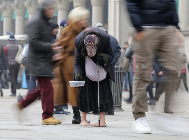 A woman begs for money amid passersby in downtown Milan on Tuesday. (AP-Yonhap News)