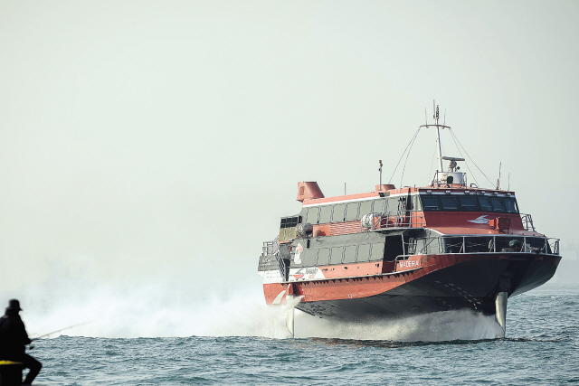 A high-speed ferry enters Victoria Harbor as a man fishes in front of a haze of pollution in Hong Kong on Wednesday. (AFP-Yonhap News)