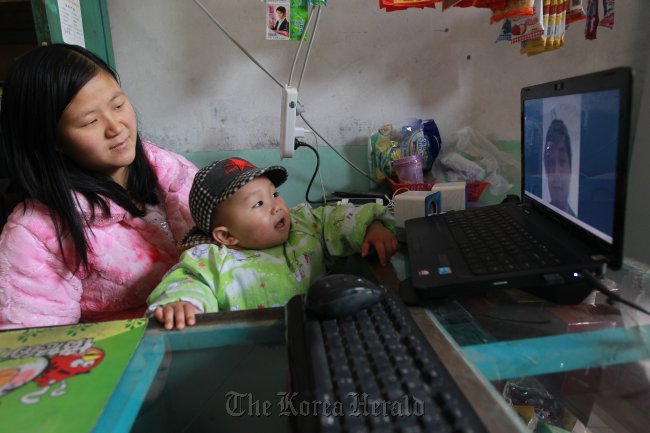 Olsen sits with his aunt in front of the computer. At 11 a.m. every day, he video chats with his parents in the U.S. (China Daily)