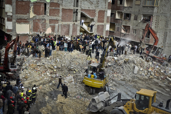 Egyptians stand in rubble after an eight-story building collapsed in Alexandria, Egypt, Wednesday. (AP-Yonhap News)