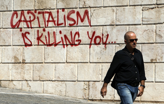 A pedestrian walks in front of graffiti in Athens. (AP-Yonhap News)