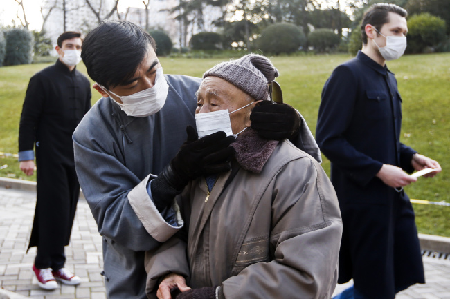 A man helps an elderly passer-by put on a mask while others hand out free masks to pedestrians in an effort to promote public awareness to use masks for protection from polluted air in Shanghai on Friday. (AP-Yonhap News)