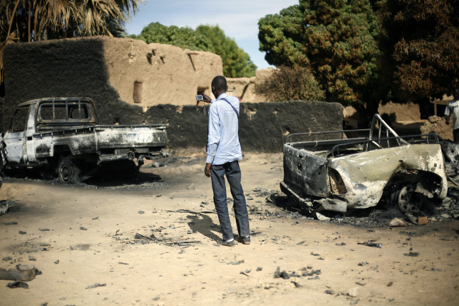 An unidentified man takes a picture of the charred remains of trucks used by radical Islamists on the outskirt of Diabaly, Mali, Monday. ( AP-Yonhap News)