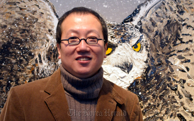 Artist Sa Suk-won poses for a photo in front of his “Dongdaemun” painting at his exhibition at Lotte Gallery in Seoul last week. (Kim Myung-sub/The Korea Herald)