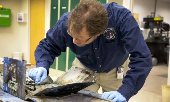 NTSB Materials Engineer examines the casing from the battery involved in the Japan Airlines Boeing 787 fire in a plane that had already landed in Boston at NTSB headquarters in Washington on Wednesday. (AP-Yonhap News)