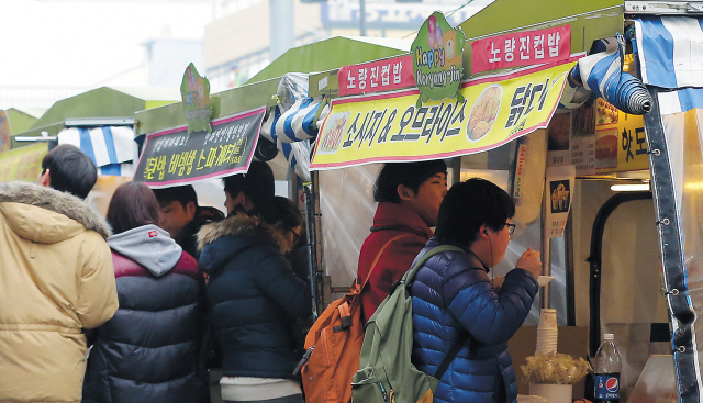 Students huddle to eat “cup bap” or cup rice, an instant and ultra-cheap meal served at food stalls in Noryangjin, a district of western Seoul packed with private academies and cheap housing known as goshiwon. (Yonhap News)