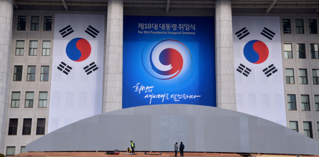 A placard and national flags hang on the building of the National Assembly Monday where Park Geun-hye will swear in as the 18th president on Feb. 25. The sign has her inauguration slogan, “Will Open the New Era of Hope.” (Park Hyun-koo/The Korea Herald)