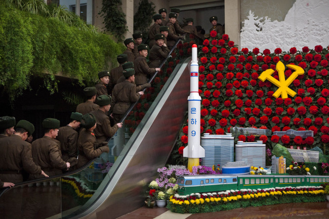 North Korean soldiers ride an escalator past a model of their country’s Unha Rocket as they enter an exhibition on Sunday in Pyongyang, where Kimjongilia flowers, named after the late North Korean leader Kim Jong-il, were on display. (AP-Yonhap News)