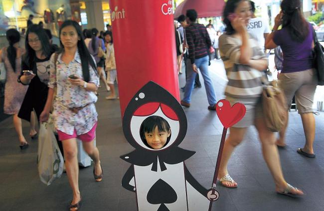 A young girl poses as the Jack of Spades while shoppers make their way past her on a busy shopping street in Singapore. Planners of Singapore envisage expanding upward, outward and downward. (AP-Yonhap News)