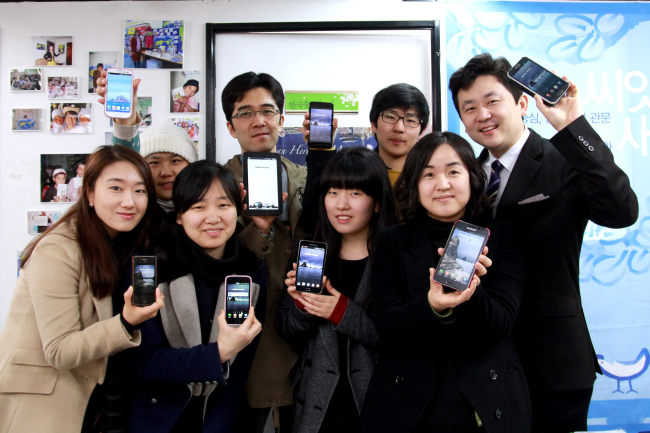 Park Ki-tae (right, back row), founder and leader of VANK, and its members hold their smartphones after changing their wallpapers into Dokdo photos. (Yonhap News)