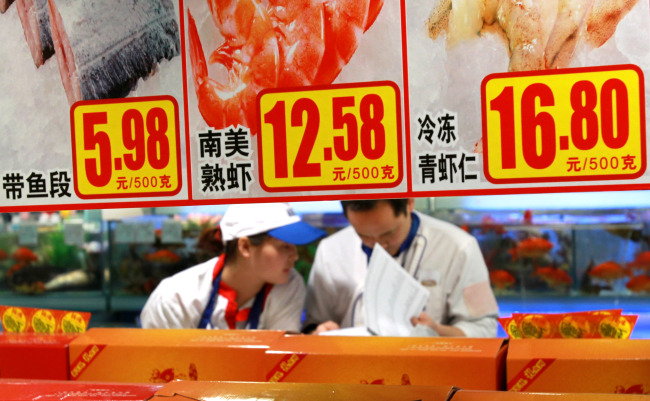 Staff members check goods behind price tags at a supermarket in Shanghai on Saturday. (Xinhua-Yonhap News)