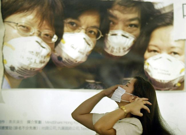 In a file picture taken in April 2003, a woman puts on a mask under a poster urging people in Hong Kong to wear them to protect against a killer outbreak of pneumonia known as SARS. (AFP-Yonhap News)