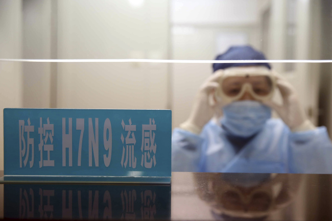 A health worker wearing protective clothing adjusts her goggles at a desk with a sign that reads “H7N9 flu prevention” at a hospital in Shanghai, China, Monday. (AP-Yonhap News)