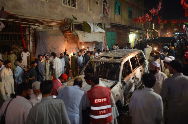 Local residents and volunteers gather around a destroyed vehicle at the site of a suicide bomb attack at an election campaign rally in Peshawar, Pakistan, Tuesday. (AFP-Yonhap News)