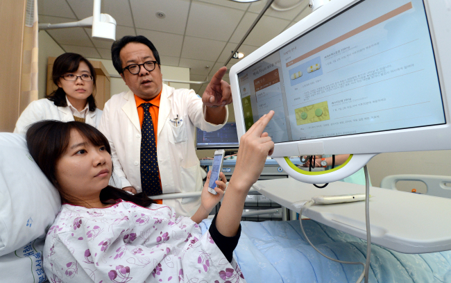 A patient and doctors use an ICT-based “smart hospital solution” program at the Seoul National University Bundang Hospital in Gyeonggi Province on Monday. Health Connect, a joint venture between SK Telecom and Seoul National University Hospital, commercialized the solution system which provides patients or visitors with various services such as submitting applications for medical checkups and paying hospital bills through digital devices. (Ahn Hoon/The Korea Herald)