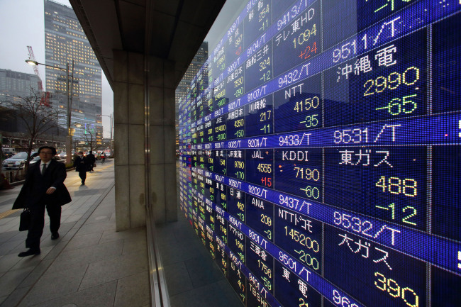 Pedestrians walk past an electronic stock board outside a security firm in Tokyo. (Bloomberg)