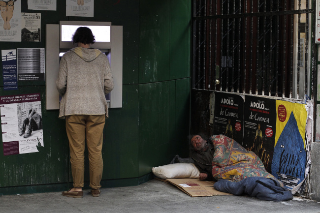 A man uses an ATM machine as a homeless man begs for alms from his makeshift bed in Madrid on Monday. (AP-Yonhap News)