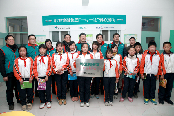 A group of executives and employees at the Chinese branches of Hana Bank and Korea Exchange Bank poses with students after setting up a library in Langfang City, Hebei province, in December 2012.