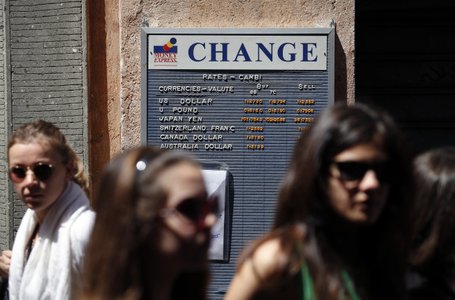 Pedestrians pass a board displaying foreign exchange rates in Rome. (Bloomberg)