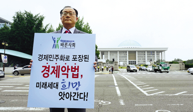 Yoo Ho-yeol, professor of North Korean studies at Korea University and chairman of the Korean Political Science Association, holds up a sign protesting moves to legislate economic democratization measures in front of the National Assembly in Seoul on Monday. Some government agencies and lawmakers are pushing for anti-chaebol policies in the name of protection of the underprivileged while conglomerates are opposing the “corporation-bashing” schemes. (Park Hae-mook/The Korea Herald)