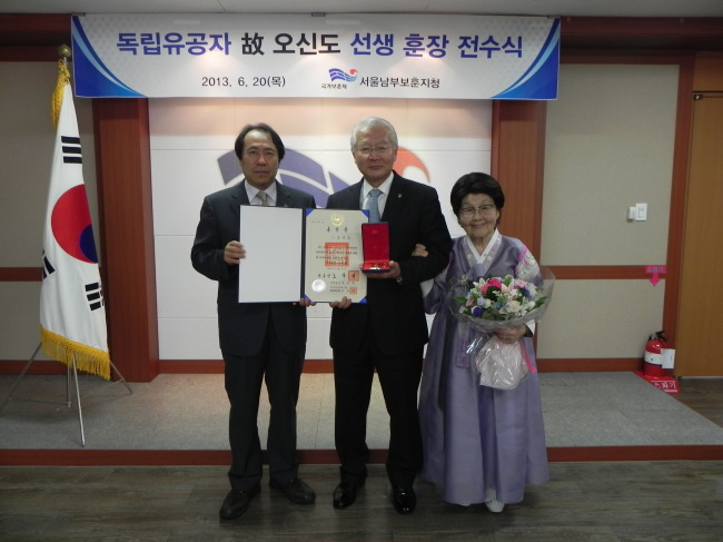 Herald Corp. senior adviser Sohn Myoung-won (center), a great grandson of independence fighter Oh Shin-do, receives a posthumous honor on her behalf from Yoon Doo-seoub (left), southern Seoul regional administrator of the Ministry of Patriots and Veterans Affairs, on Thursday. (Ministry of Patriots and Veterans Affairs)