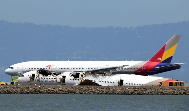 An Asiana Airlines flight enroute to South Korea takes off by the wreckage of Asiana Airlines flight 214 as it sits on runway 28L at San Francisco International Airport on Monday in San Francisco, California. (AFP-Yonhap News)