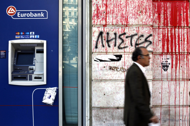 A pedestrian passes a wall covered in graffiti next to the Eurobank in Athens. (Bloomberg)