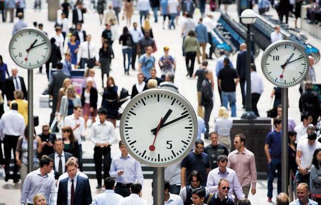 Office workers pass clocks in the Canary Wharf business and shopping district in London. (Bloomberg)