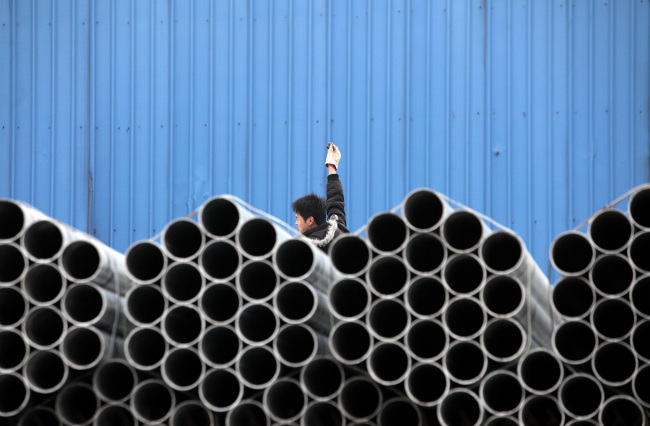 A worker stands behind stacked steel pipes at a storage yard in Shanghai. (Bloomberg)