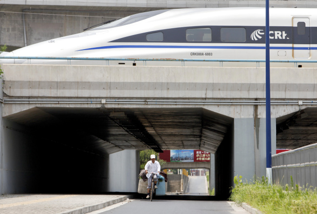 A man cycles through a tunnel under a parked high-speed bullet train at a rail maintenance center in the outskirts of Shanghai. (Bloomberg)