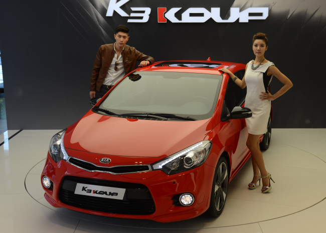 Models pose with Kia Motors’ new coupe, the K3 KOUP, at a launch in Seoul on Tuesday. (Chung Hee-cho/The Korea Herald)