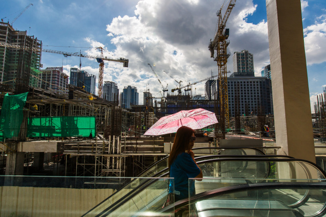 A woman carrying an umbrella rides an escalator past a construction site in the Fort Bonifacio district of Manila. (Bloomberg)