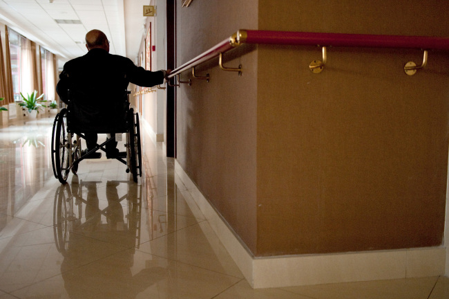 An elderly wheelchair user holds a wall-mounted bar to propel himself at the Beijing Sunshine International Care House in Beijing. (Bloomberg)