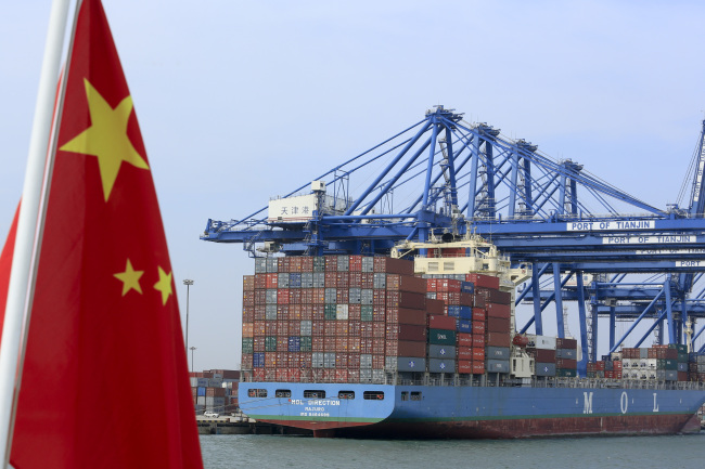 A Chinese flag flies on a vessel moving past shipping containers being unloaded at a Tianjin Port Group Co. dock in Tianjin on Thursday. (Bloomberg)