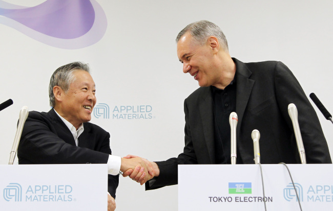 Gary Dickerson (right), chief executive officer of Applied Materials Inc., shakes hands with Tetsuro Higashi, chairman of Tokyo Electron Ltd., during a news conference in Tokyo on Tuesday. (Bloomberg)