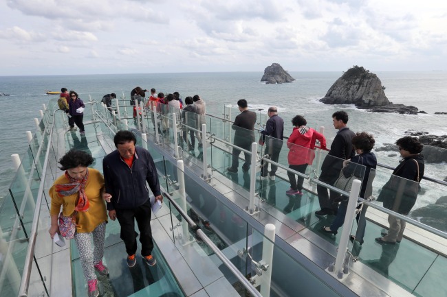 Tourists stroll on the newly opened skywalk with a view of Oryukdo Island on Friday. (Yonhap News)