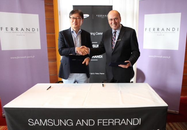 Samsung Electronics’ chief of consumer electronics business Yoon Boo-keun (left) poses with Ferrandi president George Nectoux after signing a pact in Paris over the weekend, under which the Korean conglomerate’s home appliances unit will open cooking classes at the French culinary school. (Samsung Electronics)