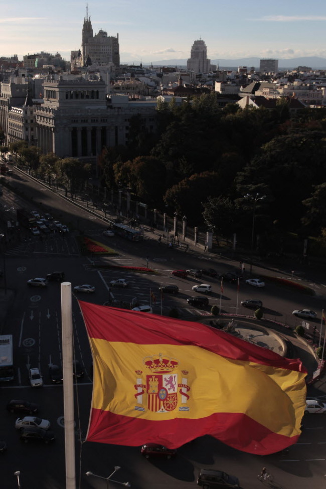 A Spanish national flag flies above the town hall as automobiles maneuver around Cibeles Square in Madrid. (Bloomberg)