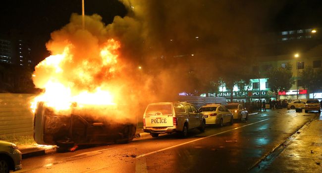 This photograph made available by The New Paper on Dec. 9, 2013 shows a police car (left) flipped on it side on fire after rioters went on a rampage in Singapore's Little India district late on Dec. 8. (AFP-Yonhap News)